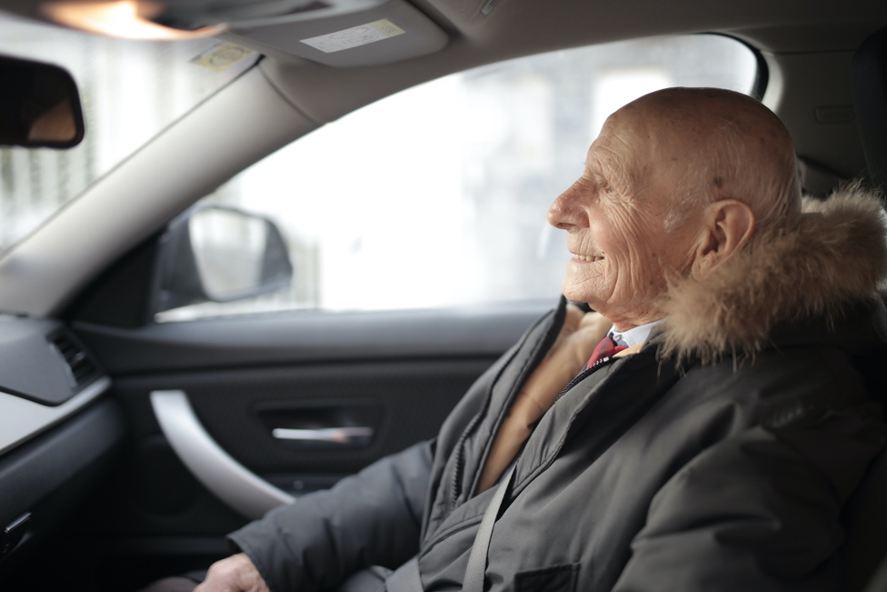 An older man sits happily in a vehicle.